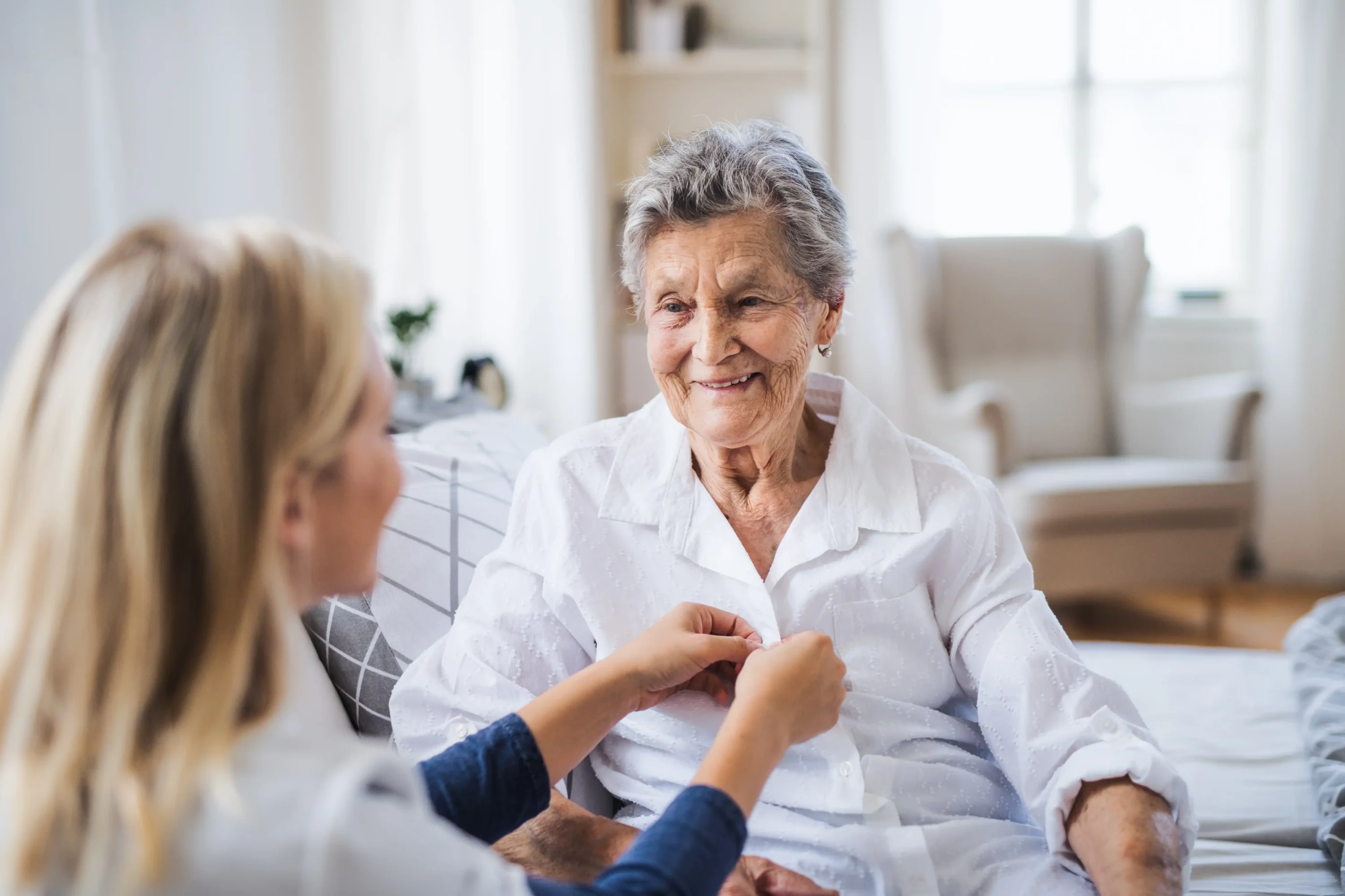 Caregiver helping elderly woman button shirt at home