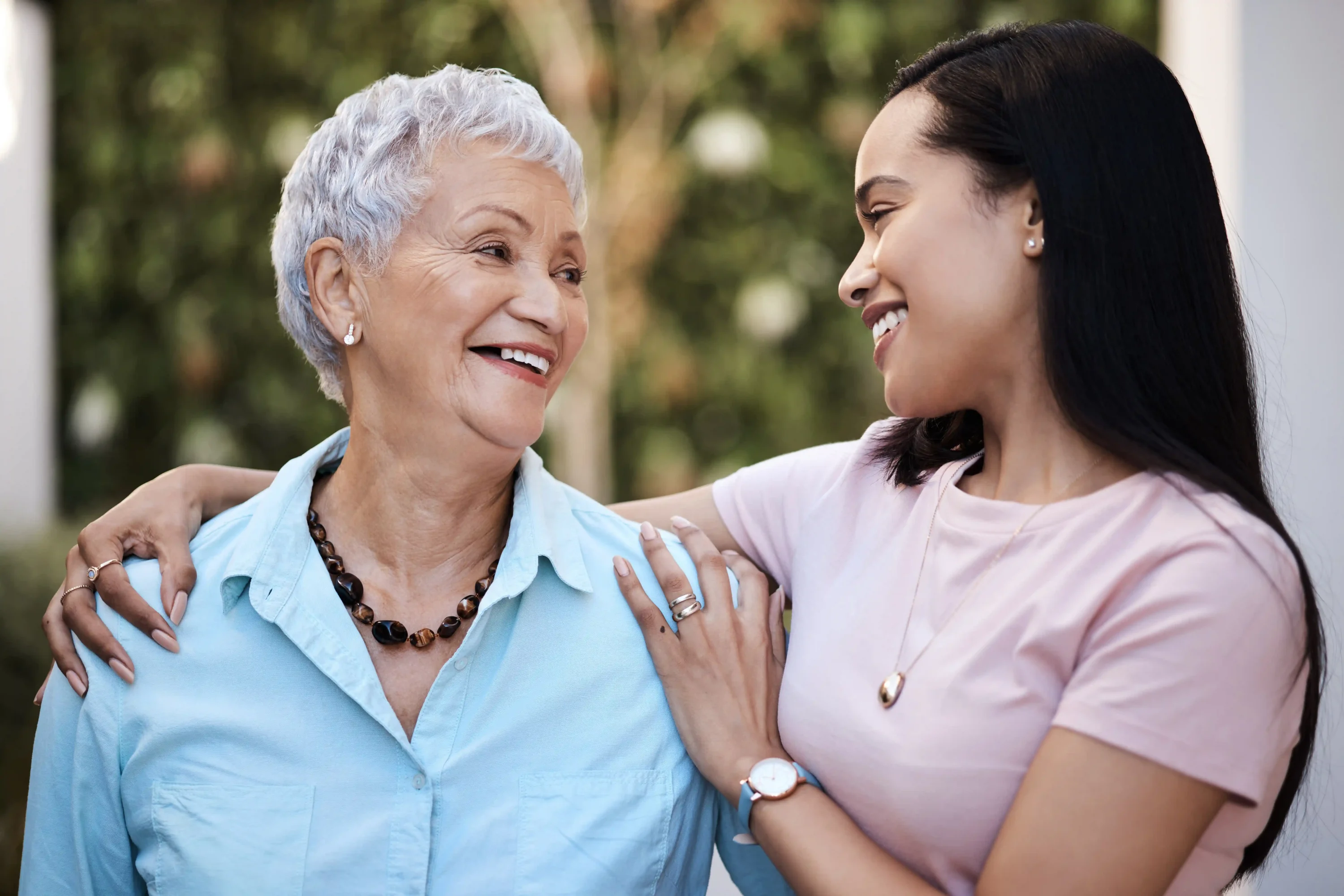 Daughter embracing smiling elderly mother outdoors