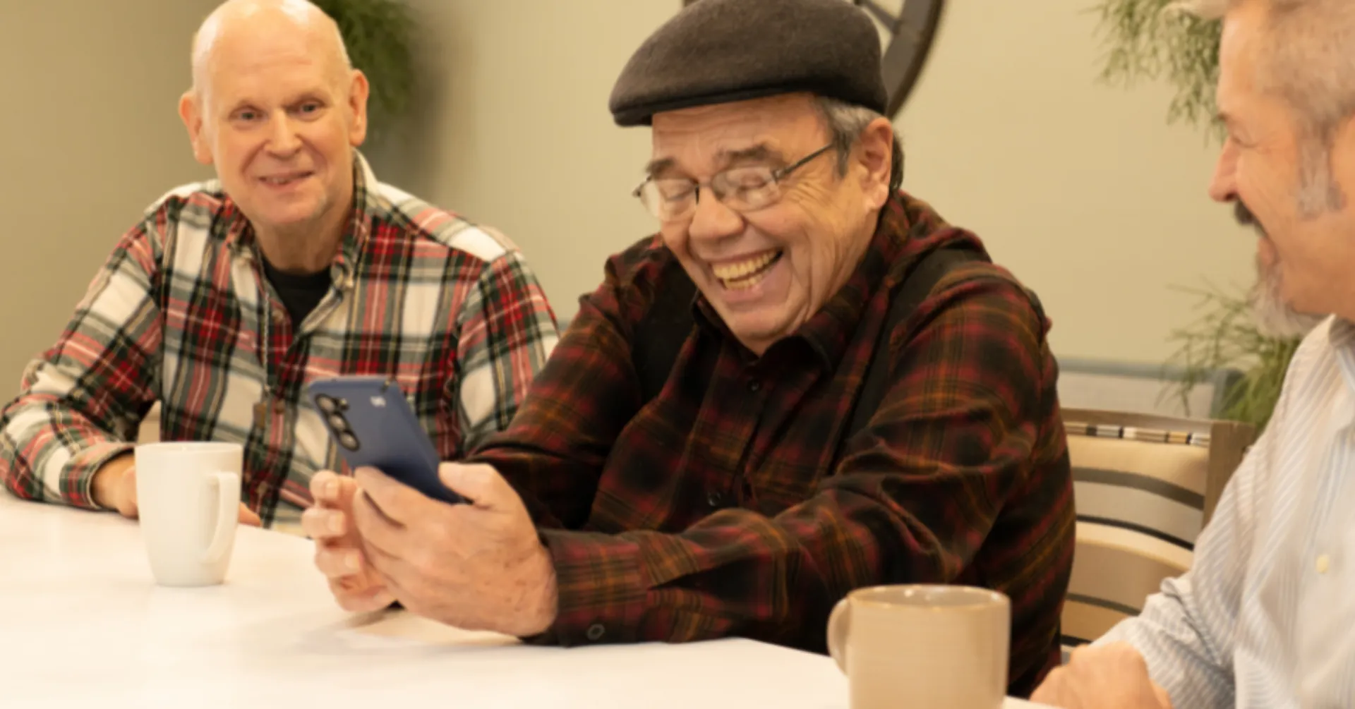Three older men laughing at smartphone together