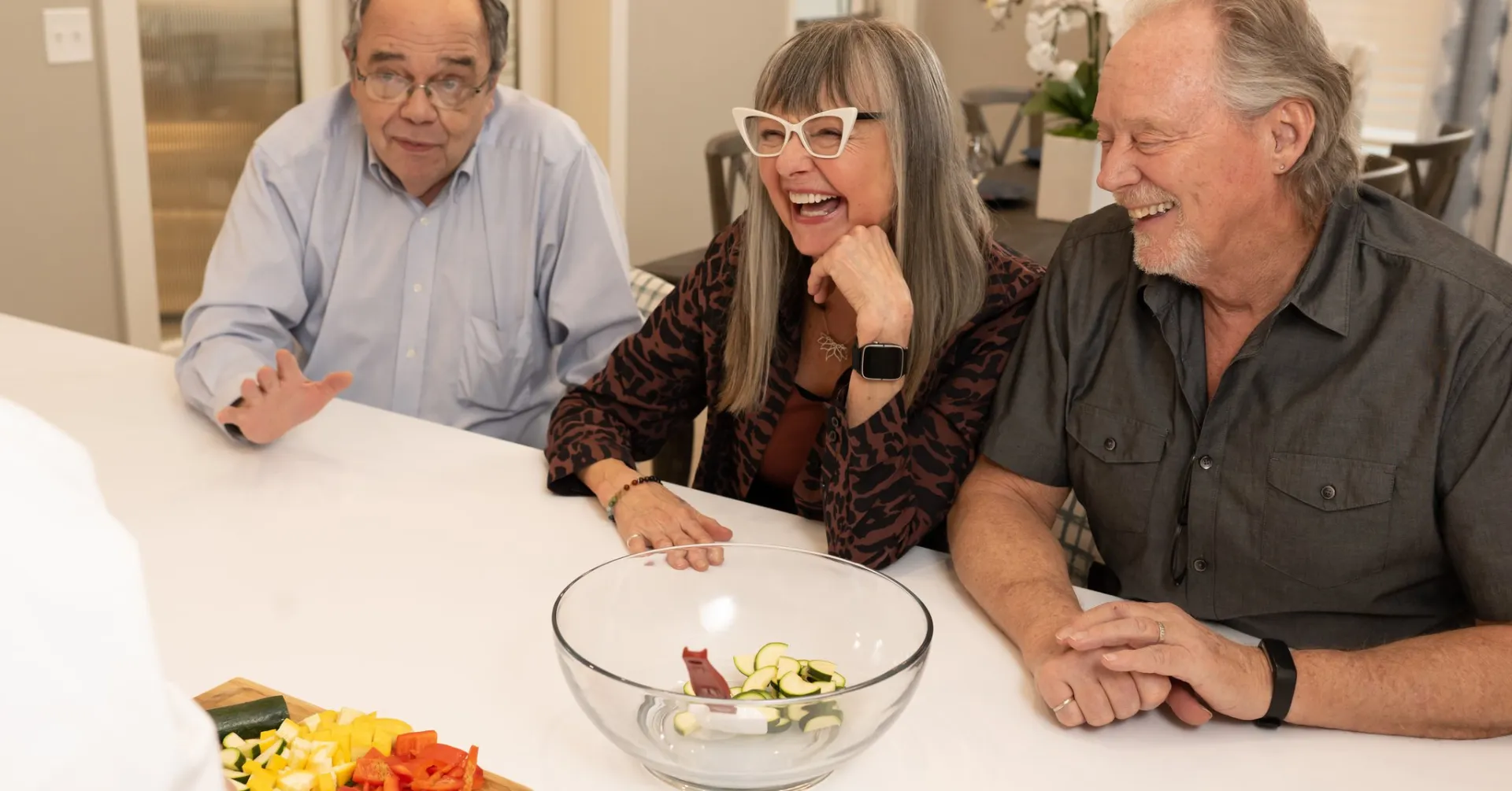 Three seniors laughing at table with fresh vegetables