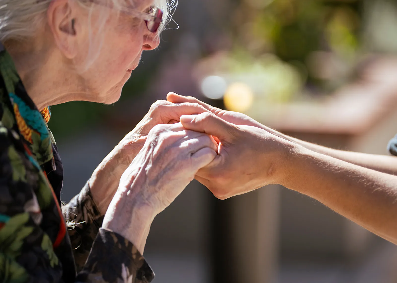 Elderly woman holding caregiver's hands outdoors