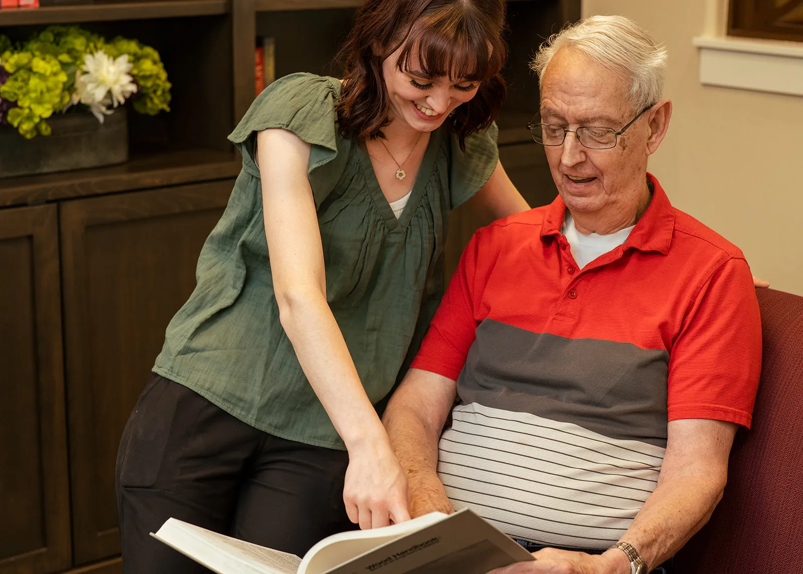 Young woman helping elderly man read book