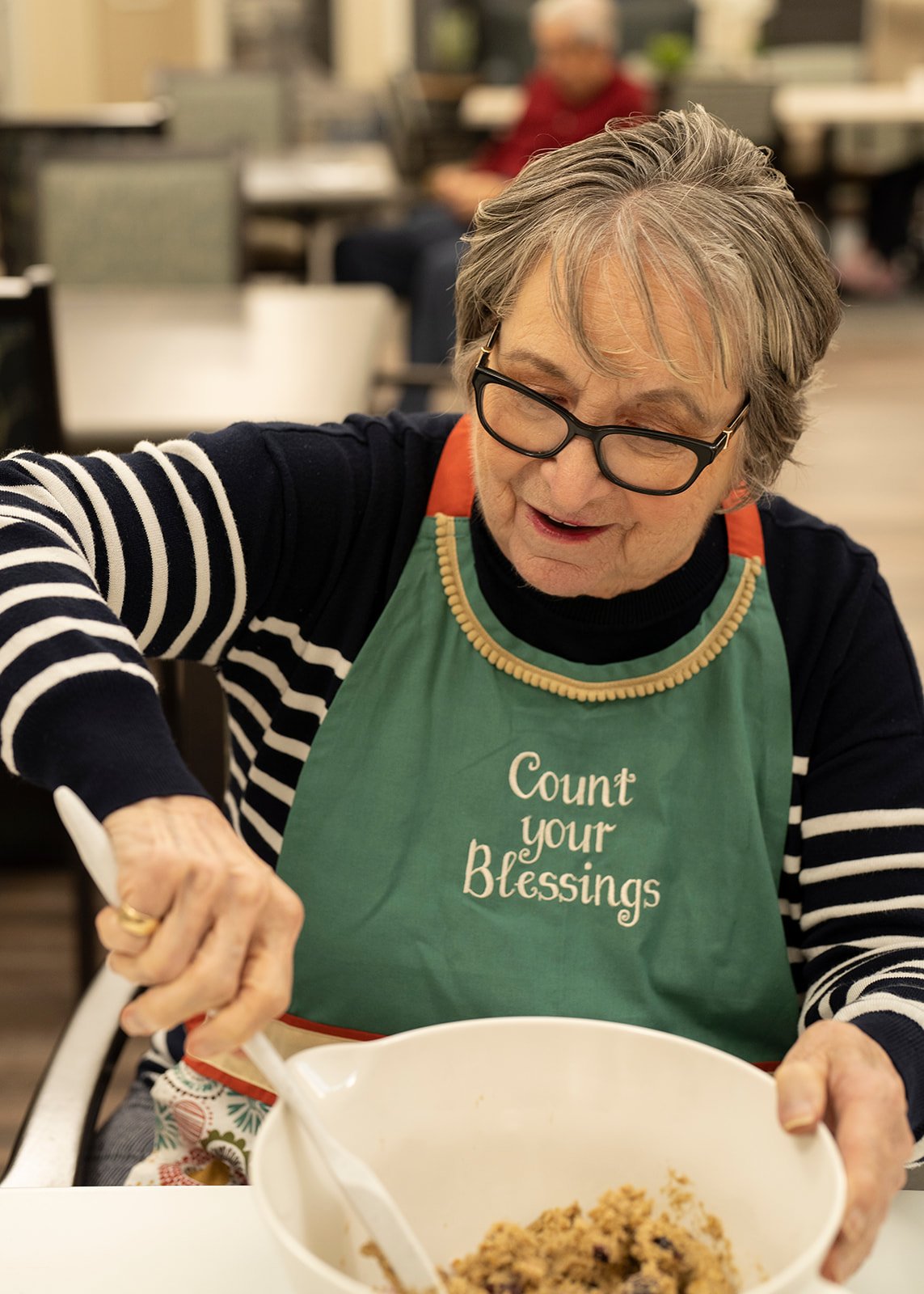 Elderly woman mixing batter in green apron