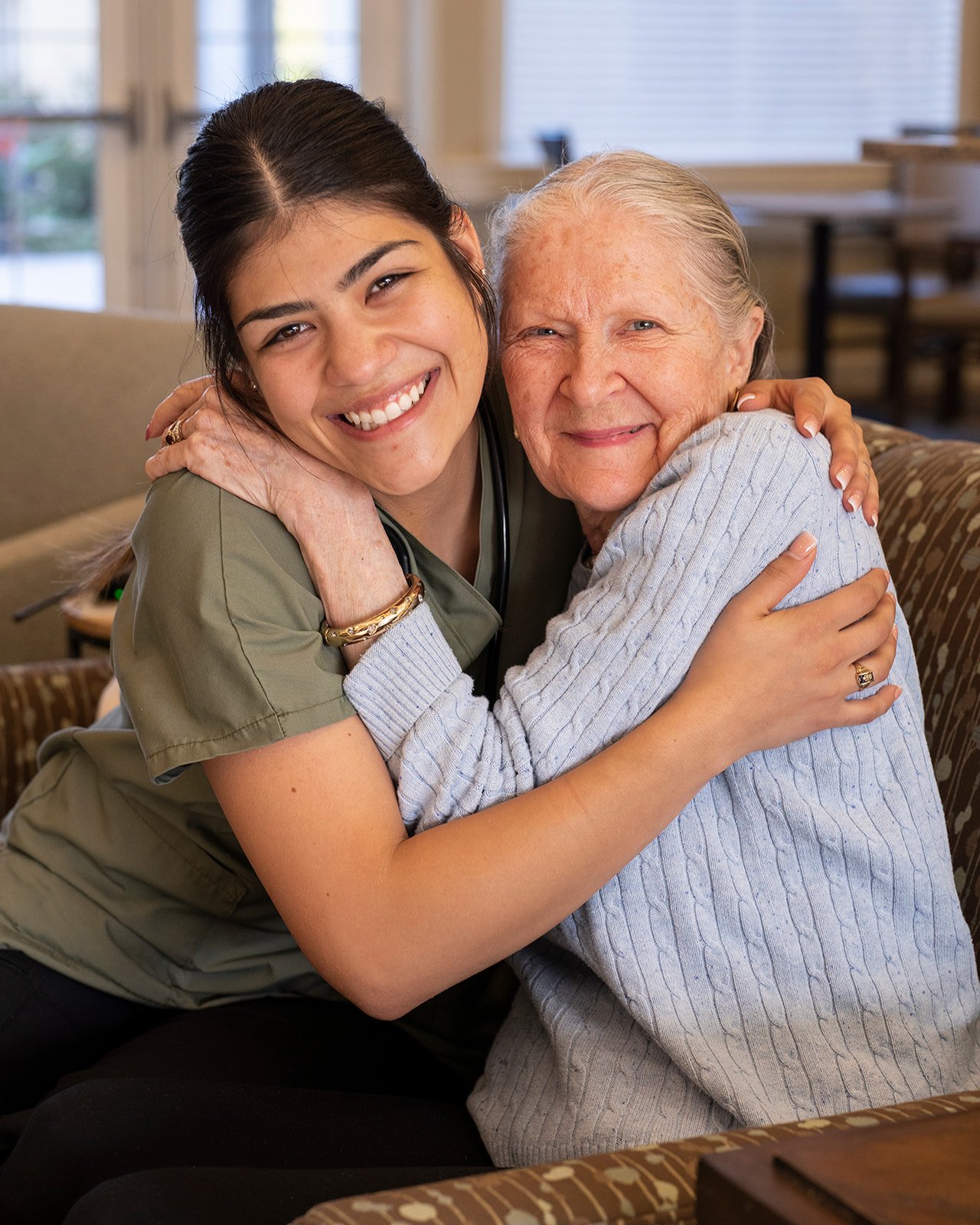 Caregiver hugging smiling elderly woman indoors